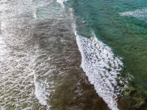 Ilmakuva kristallinkirkkaasta merestä aaltoineen ja surffareineen. Playa De La Canteria (s. Atlantin valtameri, aallot törmäävät rantaan auringonlaskun aikaan, taustavalo. Orzola, Lanzarote, Kanariansaaret. Espanja
 - Valokuva, kuva
