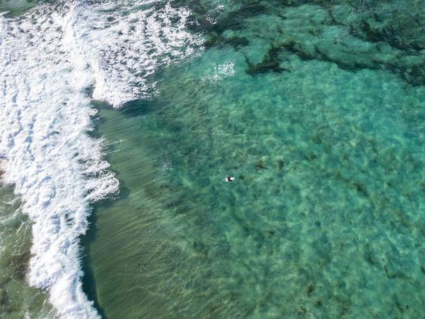 Ilmakuva kristallinkirkkaasta merestä aaltoineen ja surffareineen. Playa De La Canteria (s. Atlantin valtameri, aallot törmäävät rantaan auringonlaskun aikaan, taustavalo. Orzola, Lanzarote, Kanariansaaret. Espanja
 - Valokuva, kuva