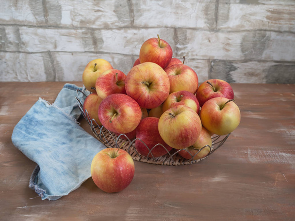 A lot of apples in a metal wicker basket close-up on a light wooden background, denim napkin - Photo, Image