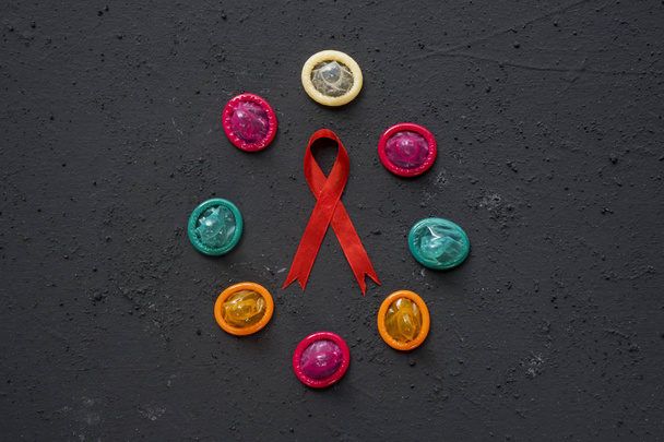 Vista superior de uma fita vermelha com preservativos coloridos em forma de círculo na mesa
 - Foto, Imagem