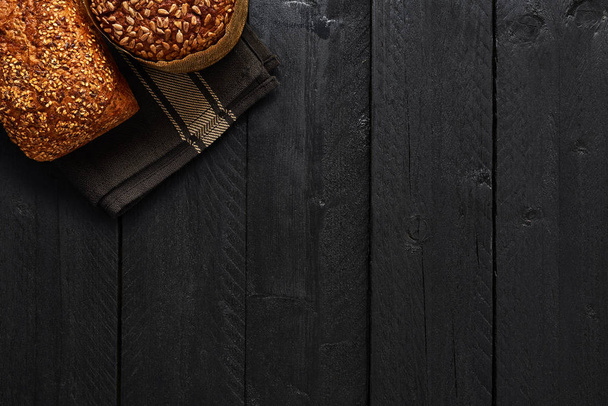 Various crusty whole wheat bread on black wooden table. Top view with copy space for text, menu or recipes. - Foto, imagen