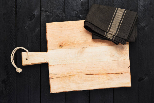 Top view of chopping board with dishtowel on black wooden background with copy space. - Foto, afbeelding