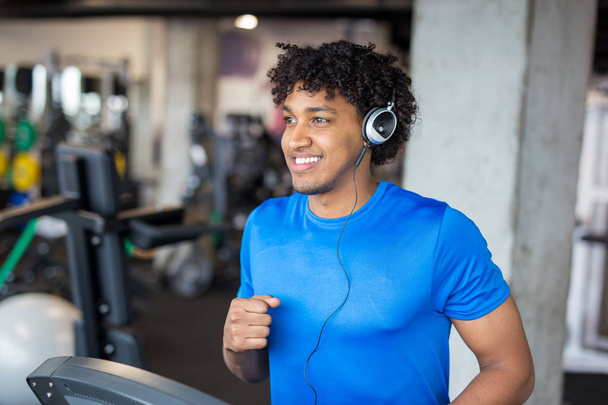 Pohledný americký muž cvičit v tělocvičně při poslechu hudby na běžeckém pásu - Fotografie, Obrázek