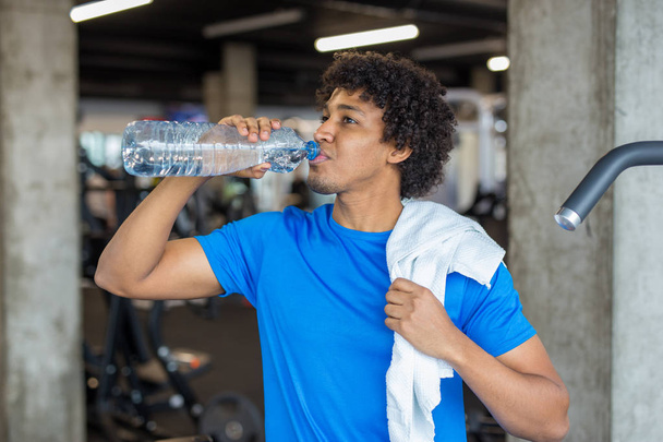 Beau jeune homme buvant de l'eau à la salle de gym regardant loin de la caméra
 - Photo, image