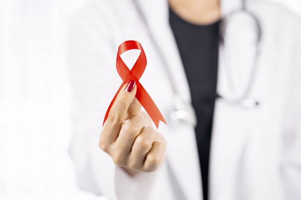 Closeup of a young female doctor showing red ribbon. world AIDS day concept - Foto, imagen