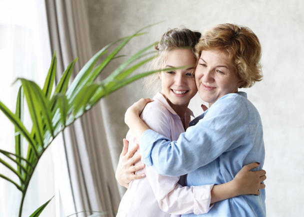 lifestyle  and people concept: Happy senior mother embracing adult daughter laughing together, smiling excited aged older lady hugging young woman, family life - Photo, image