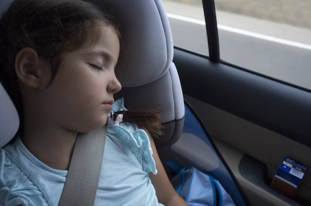 Menina criança dormindo em um assento de segurança infantil durante a viagem. Ela tem um batido de tijolo na porta do carro.
 - Foto, Imagem