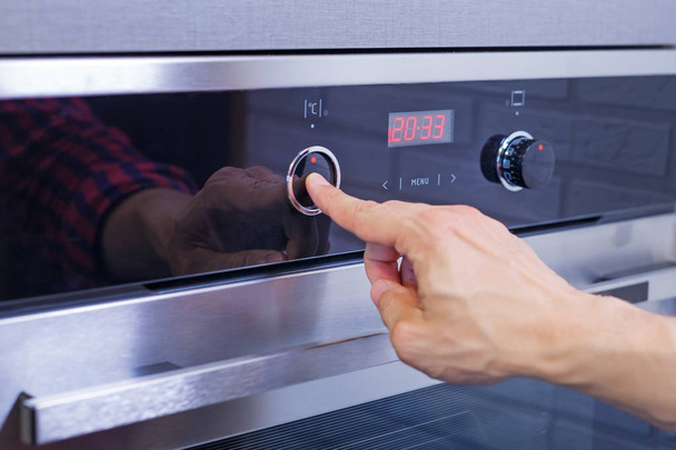 Человек ручной настройки режима приготовления пищи на электрической печи. Мужской палец нажать кнопку на панели управления на духовке, закрыть
 - Фото, изображение