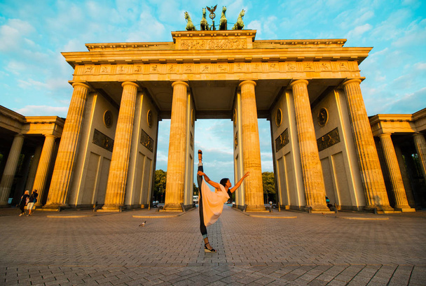 Berlin, Germany - 06.09.2018. Famous Brandenburger Tor (Brandenburg Gate) in beautiful golden morning light at sunrise with a black nice dancing woman. - Photo, image