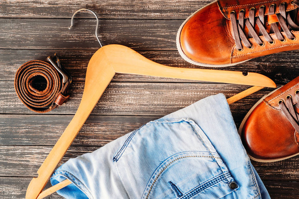 Brown leather casual shoes, jeans on hangerand belt on a wooden background top view. Fashion concept - Foto, imagen