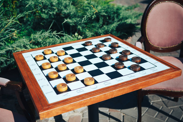Настольные игры на улице на деревянном столе и мягких стульях. Чекеры
 - Фото, изображение