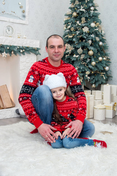happy dad and daughter in red sweaters sitting on the carpet near the fireplace decorated for Christmas eve - Фото, зображення