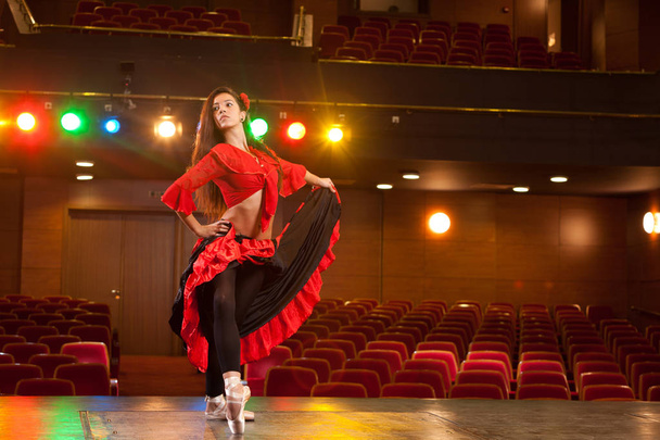 Красивая брюнетка-танцовщица, одетая в красное платье, исполняющая танцевальную позу на сцене
. - Фото, изображение