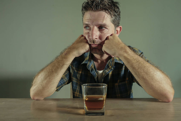 isolated portrait of young drunk addict and alcoholic man drinking whiskey glass intoxicated looking wasted resisting temptation to his alcohol addiction and abuse problem in alcoholism concept  - Фото, изображение