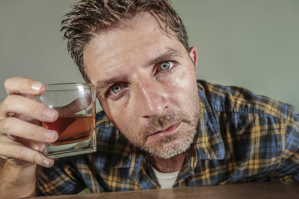 young attractive wasted and depressed addict and alcoholic man with whiskey glass thoughtful and sad failing resisting temptation to drink falling into alcohol abuse addiction and alcoholism problem  - Foto, afbeelding