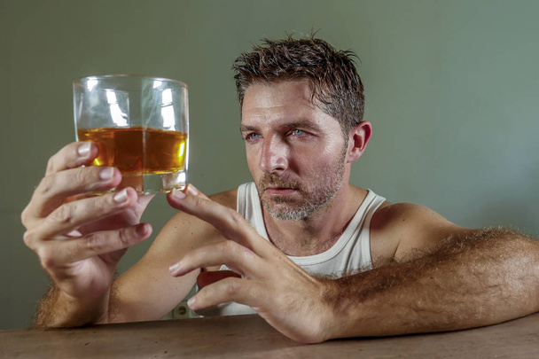 young wasted and depressed alcohol addict man in dirty singlet drinking glass of whiskey feeling desperate suffering alcoholism problem and booze addiction on isolated background in alcoholic concept - Φωτογραφία, εικόνα