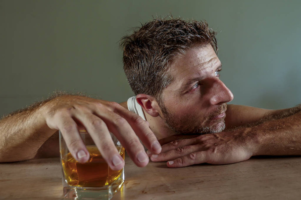 young wasted and depressed alcohol addict man in dirty singlet drinking glass of whiskey feeling desperate suffering alcoholism problem and booze addiction on isolated background in alcoholic concept - Photo, image