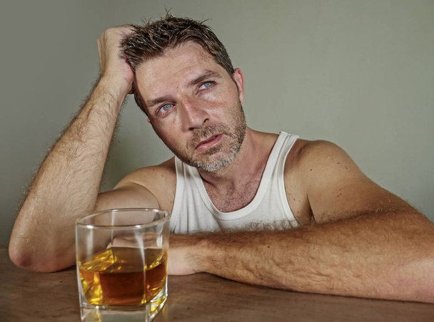 young wasted and depressed alcohol addict man in dirty singlet drinking glass of whiskey feeling desperate suffering alcoholism problem and booze addiction on isolated background in alcoholic concept - Photo, image