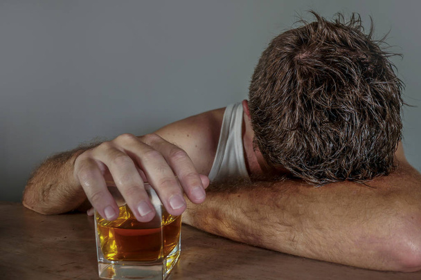 young wasted and depressed alcohol addict man in dirty singlet drinking glass of whiskey feeling desperate suffering alcoholism problem and booze addiction on isolated background in alcoholic concept - Fotó, kép