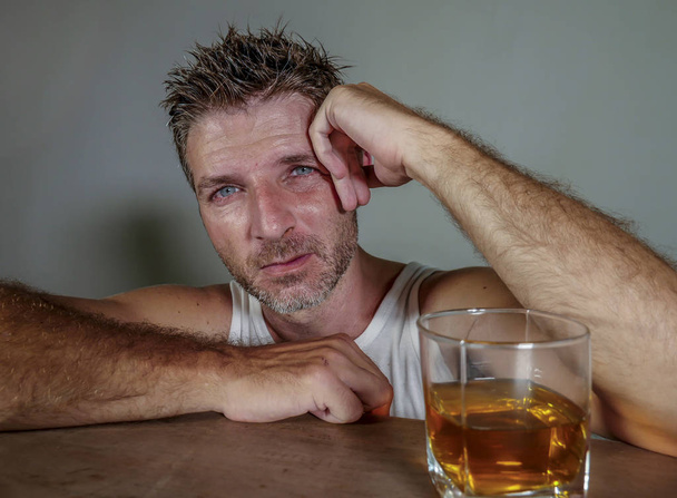 young wasted and depressed alcohol addict man in dirty singlet drinking glass of whiskey feeling desperate suffering alcoholism problem and booze addiction on isolated background in alcoholic concept - Фото, изображение