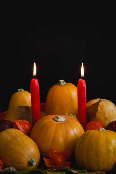 Halloween thanksgiving autumn still life composition with pumpkins apples dry leaves physalis red burning candles on dark background. Table decoration concept vertical orientation close up copy space. - Foto, Imagen