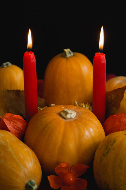 Halloween thanksgiving autumn still life composition with pumpkins apples dry leaves physalis red burning candles on dark background. Table decoration concept vertical orientation close up copy space. - Photo, image