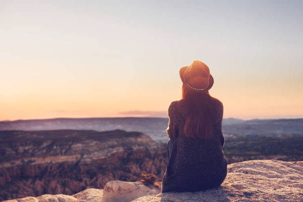 ein Blick von der Rückseite eines Mädchens mit Hut sitzt auf einem Hügel und bewundert die schöne Aussicht. - Foto, Bild