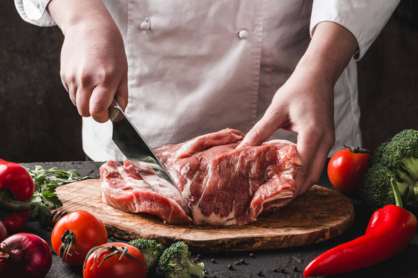 Šéf Řezník krájí vepřové maso nožem na kuchyni, vaří jídlo - Fotografie, Obrázek