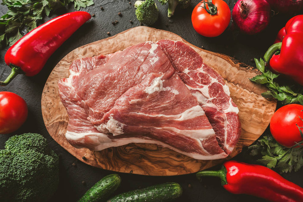 Сырое мясо, говяжий стейк на разделочной доске на черном фоне с ингредиентами для приготовления пищи. Вид сверху
 - Фото, изображение