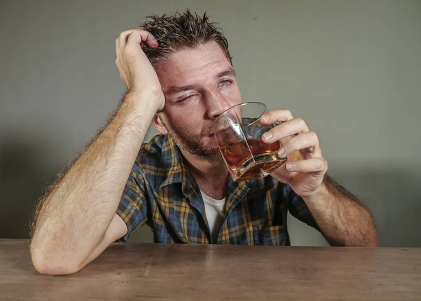 young attractive wasted and depressed addict and alcoholic man with whiskey glass thoughtful and sad failing resisting temptation to drink falling into alcohol abuse addiction and alcoholism problem  - 写真・画像