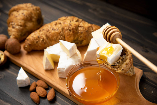 slices of cheese brie or camembert with croissants, honey and nuts on board for cutting, on dark wooden background - Foto, imagen