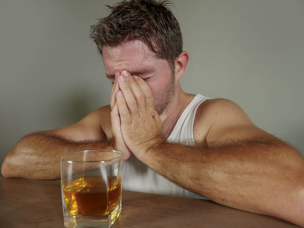 young wasted and depressed alcohol addict man in dirty singlet drinking glass of whiskey feeling desperate suffering alcoholism problem and booze addiction on isolated background in alcoholic concept - Foto, immagini