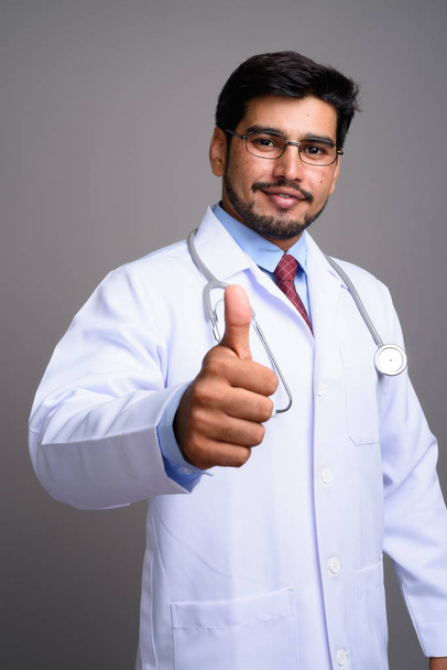Young handsome bearded Persian man doctor against gray backgroun - Photo, Image
