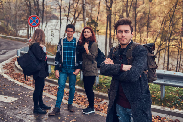 Група молодих туристів, що стоять на узбіччі дороги в прекрасному осінньому лісі
. - Фото, зображення