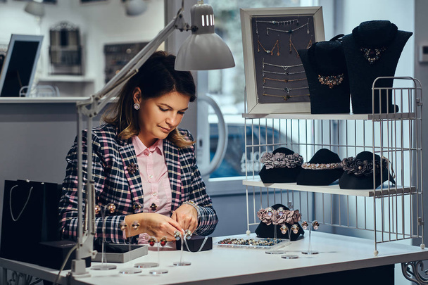Vrouw verkoper pakt kostbare oorbellen in een vak voor haar cliënt in een luxe sieraden winkel. - Foto, afbeelding