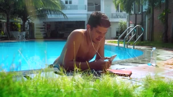 guy surfs internet over smartphone by pool barrier - Materiał filmowy, wideo