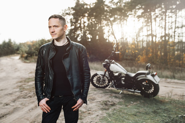 Handsome rider guy in black biker jacket on classic style cafe racer motorcycle at sunset. Bike custom made in vintage garage. Brutal fun lifestyle. - Foto, immagini