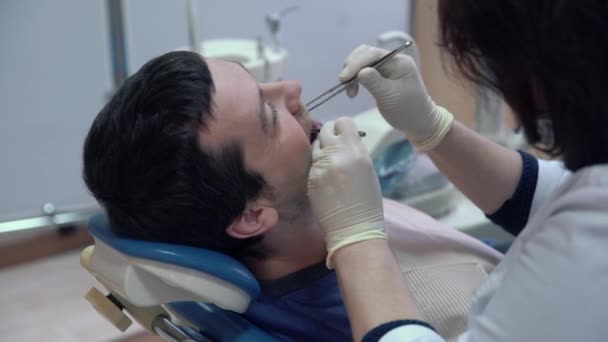 A dentist woman in a sterile mask and clothes performs procedures in the patients mouth with medical instruments. Dental treatment in a dental clinic. Health concept. - Metraje, vídeo