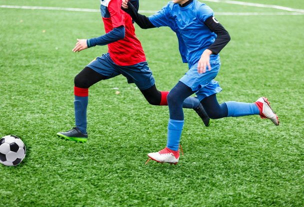 équipes de football garçons en rouge, bleu vêtements de sport jouer au football sur le terrain vert. Des garçons qui dribblent. dribbler les compétences. Jeu d'équipe, entraînement, mode de vie actif, passe-temps, sport pour enfants concept
 - Photo, image