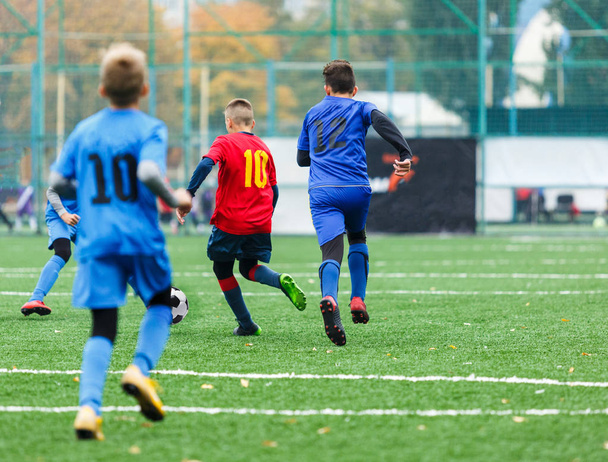 drużyny piłkarskie - chłopcy w czerwony, niebieski odzież sportowa grać w piłkę na zielonym polu. chłopcy dryblingu. umiejętności dryblingu. Zespół gra, szkolenia, aktywny tryb życia, hobby, sport dla dzieci koncepcja - Zdjęcie, obraz