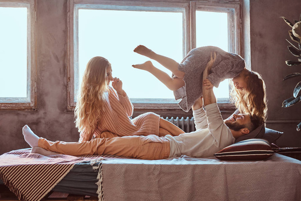 Мама, тато і дочка в ліжку. Батько, граючи з чарівною донькою в спальні. - Фото, зображення