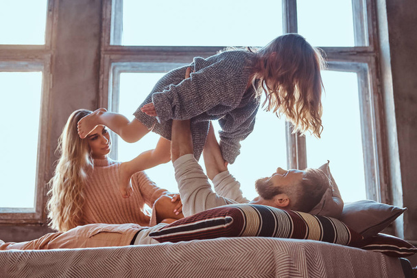 Mamá, papá e hija en la cama. Padre jugando con adorable hija en el dormitorio
. - Foto, imagen