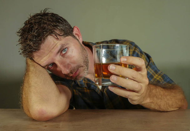 isolated portrait of young messy depressed alcoholic man having a drink looking at whiskey glass falling in temptation of alcohol abuse in addiction suffering alcoholism problem - Valokuva, kuva