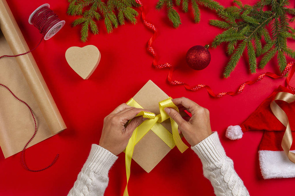 Christmas gift wrapping. Womans hands packing Christmas present box on red table background - Foto, Bild