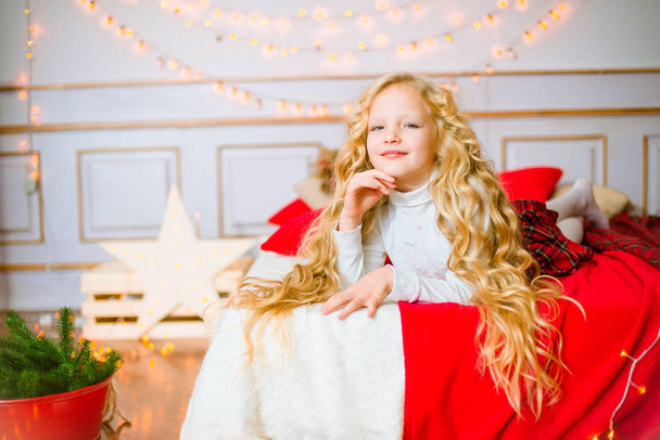 Little girl with blond long curly hair at Christmas morning.Merry Christmas.Little girl rejoices to the Christmas gift - 写真・画像