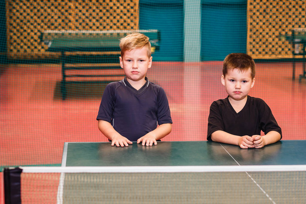 two serious boy in a sports uniform standing behind a table tennis table indoors - Foto, immagini