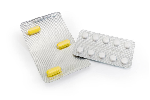 Две упаковки волдырей с тремя длинными желтыми таблетками и круглыми белыми таблетками на белом фоне
 - Фото, изображение