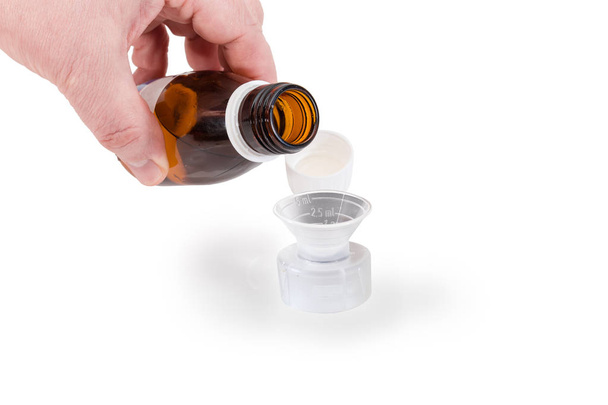 Ölçme kupa beyaz zemin üzerine tıp üzerinde insan elinde tıbbi karışımı ile açık küçük kahverengi şişe - Fotoğraf, Görsel