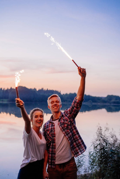 Young couple with sparklers celebrating holiday at sunset - Valokuva, kuva