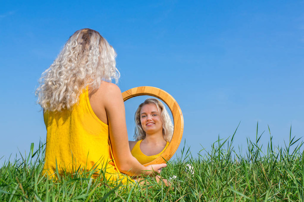 Sarışın bir kadın ona ayna görüntüsü dışında bakarak oturur - Fotoğraf, Görsel